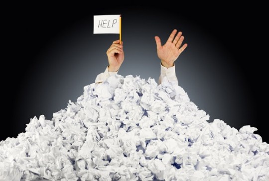 Person under crumpled pile of papers with hand holding a help si